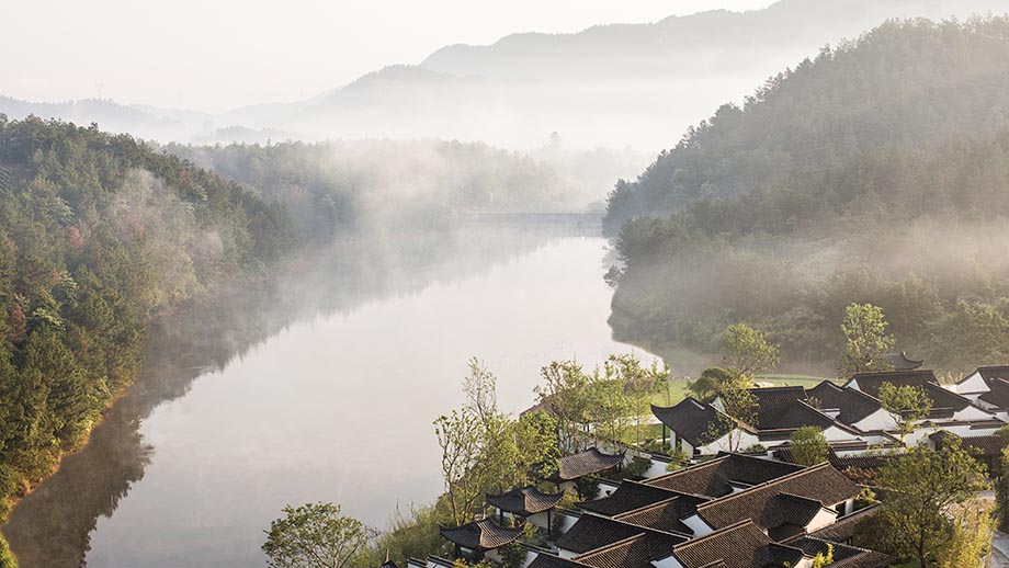 Mist shrouds a serene lakeside landscape with Banyan Tree Anji Resorts nestled among lush hills.