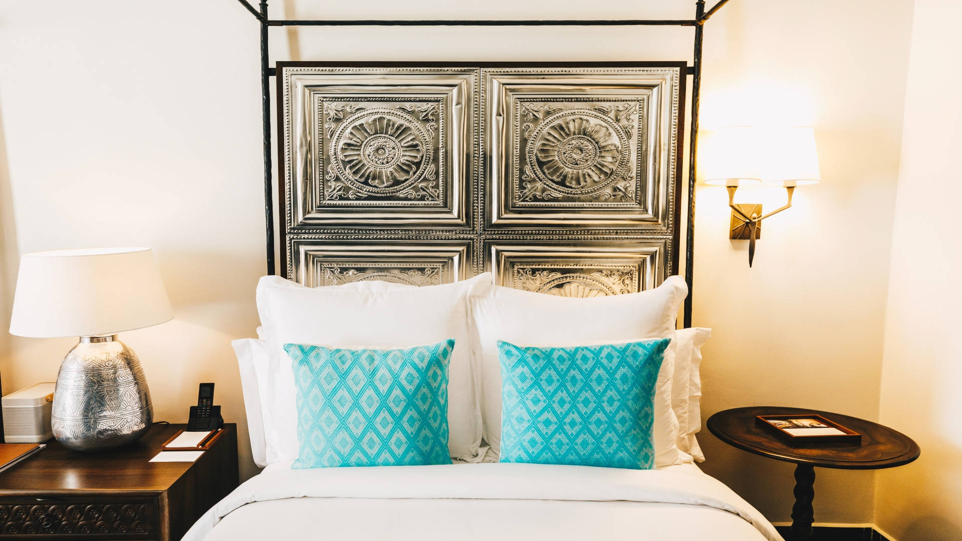 Luxurious accommodation bed with teal pillows at Banyan Tree Puebla, framed by ornate headboard and stylish lighting.