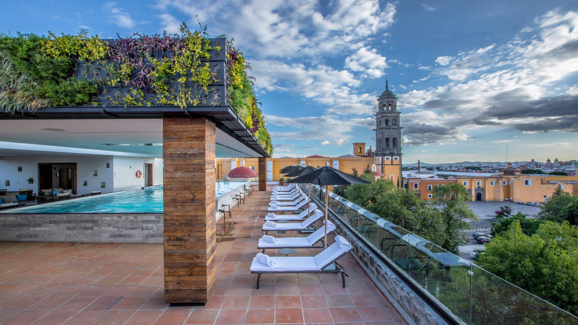 Rooftop pool bar at Banyan Tree Puebla with lounge chairs, cityscape, and distant bell tower view.