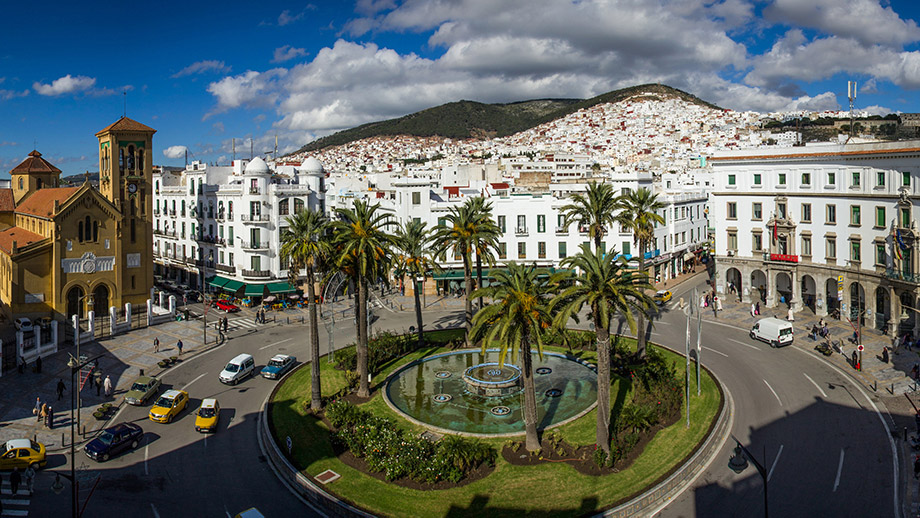 Roundabout with palm trees and fountain, surrounded by historic buildings, near Banyan Tree Tamouda Bay.