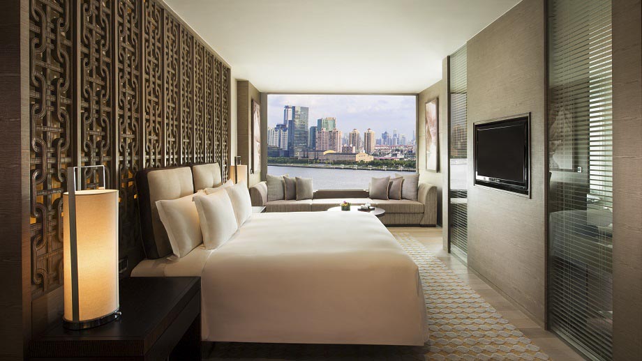 Luxurious Banyan Tree Shanghai room with elegant bed, sofa seating, window view of urban skyline.